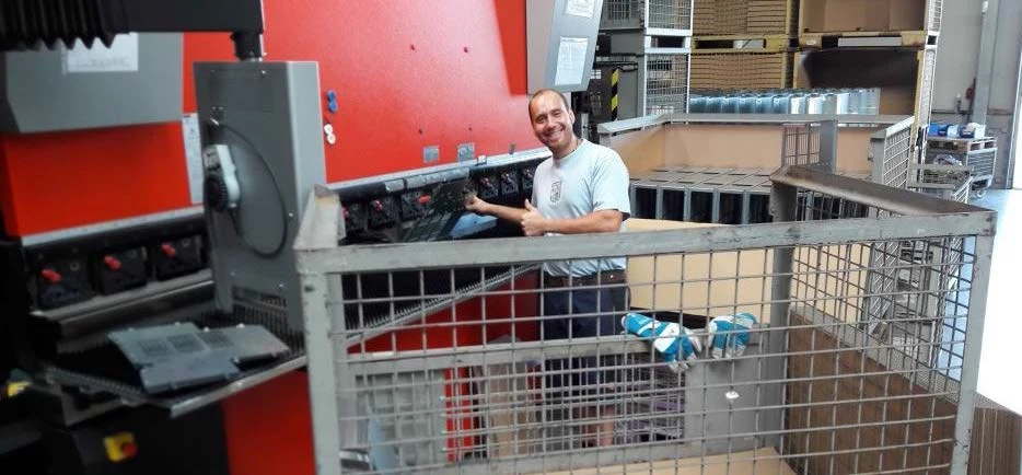 Mitarbeiter an einer Abkantpresse mit Gitterbox voller Biegeteile