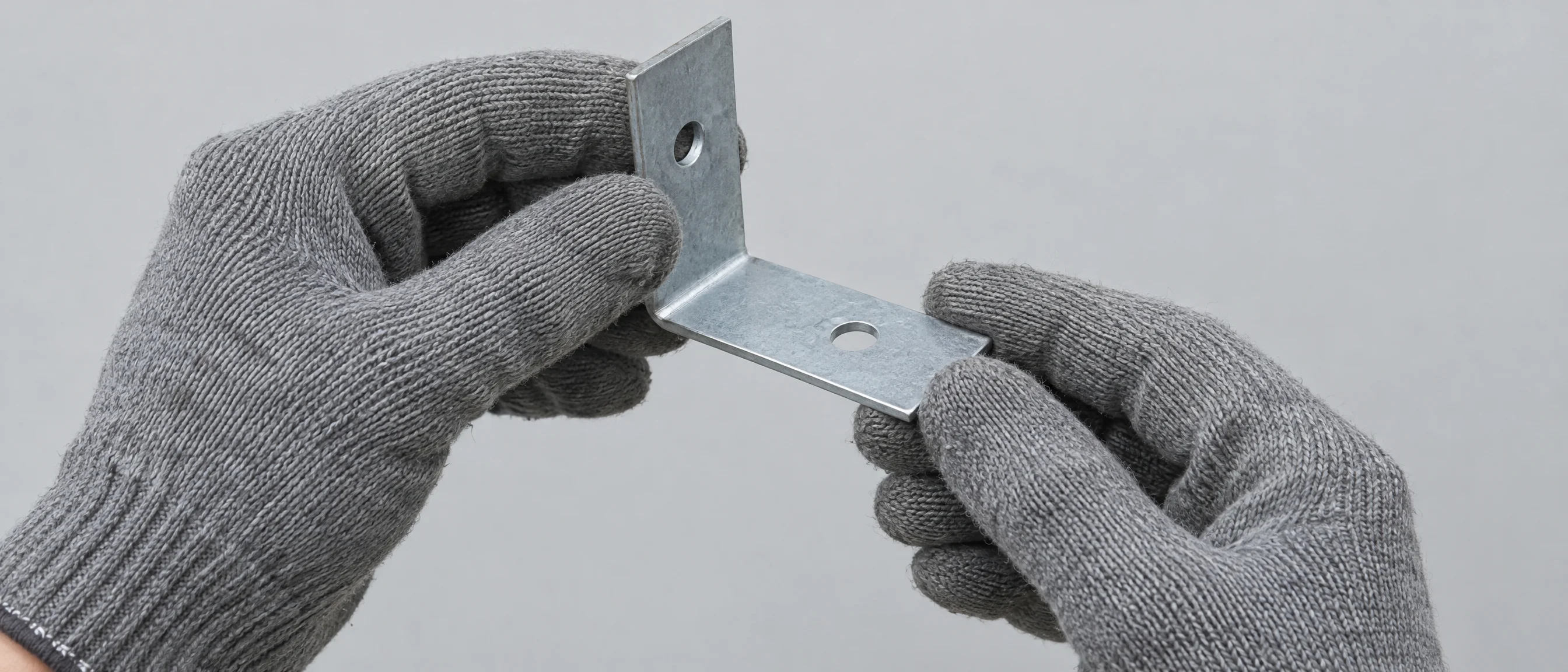 Hände in Arbeitshandschuhen prüfen einen gekanteten Winkel aus verzinktem Blech